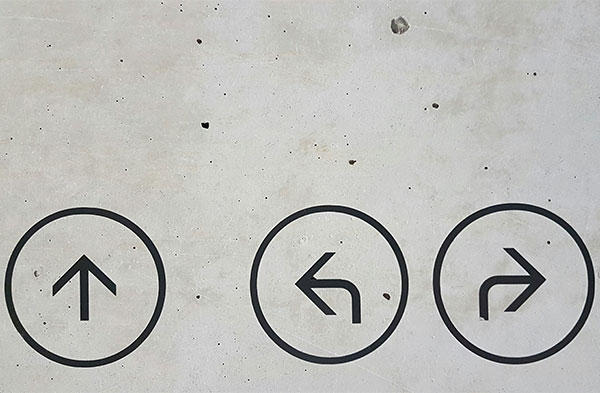 A cement wall with arrows in circles pointing in different directions (Unsplash/Marianne Bos)