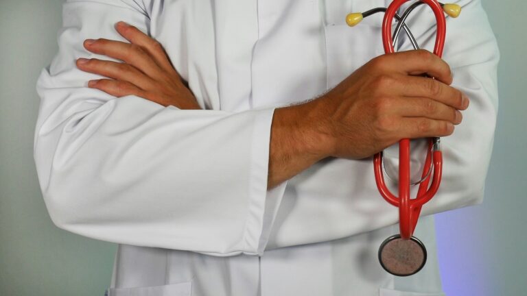 The torso of a person in a white doctor's coat holding a stethoscope with their arms cross. (Unsplash/Online Marketing)